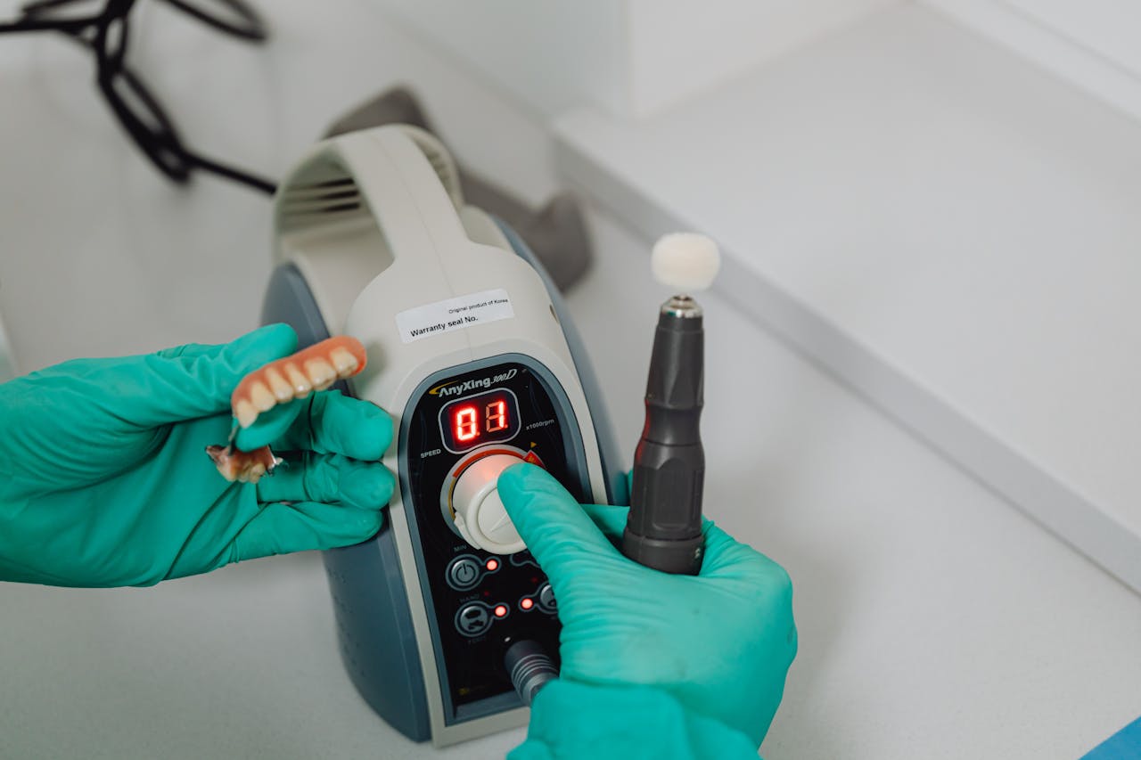 Close-up of dental technicians hands working with denture and medical machine in a lab.