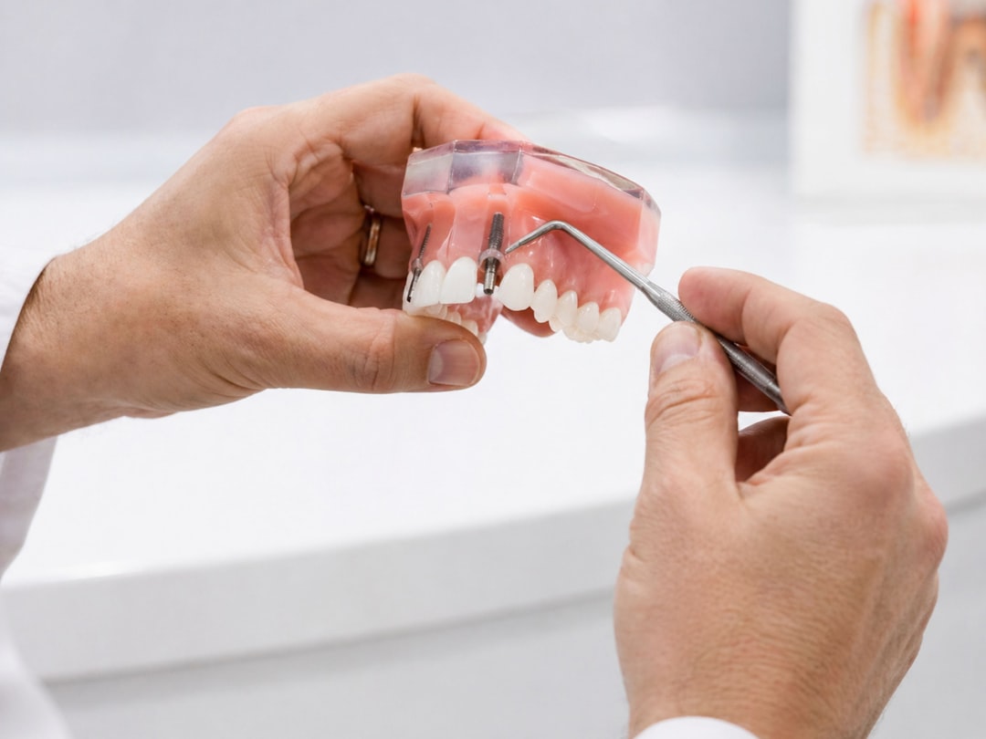 A dentist uses a dental probe to point at a screw implant on a denture model, showing false teeth and oral treatment details in a clinical dentistry setting.
